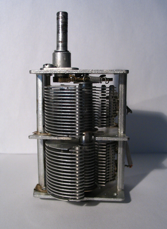 Figure 7 — An air-variable tuning capacitor, the meshing rotor and stator plates plainly visible. A single knob rotates the rotor to tune the set. Source: photograph by "Solaris2006", via Wikimedia…