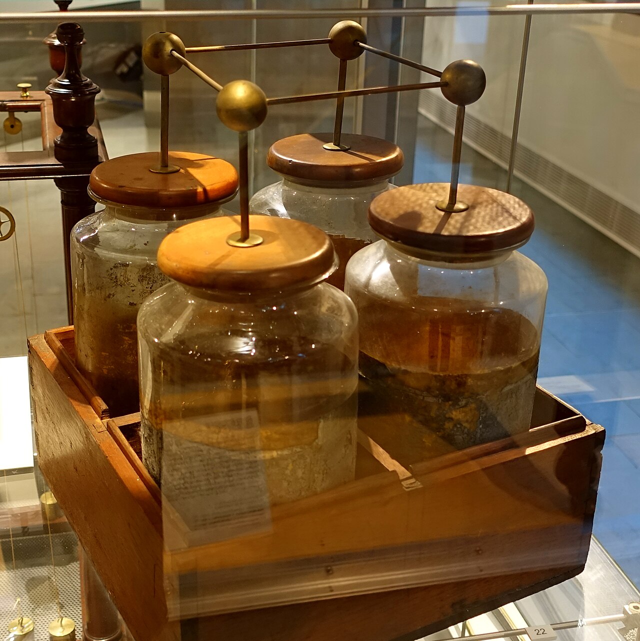 Figure 1 — A "battery" of four Leyden jars, English or American, early 1800s, in the Putnam Gallery at Harvard. Franklin coined the word "battery" for exactly this: jars wired in parallel to store …