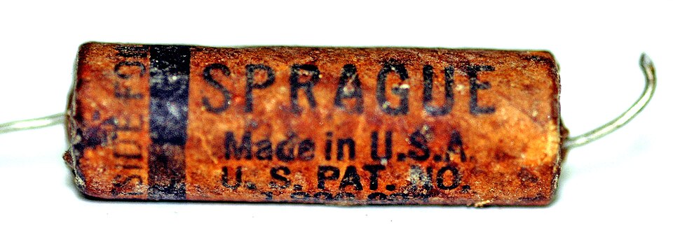 Figure 6 — A vintage Sprague wax-paper capacitor, cracked and leaking after decades in a tube radio. Rolled foil-and-paper "condensers" like this were the workhorse of early electronics — and the r…
