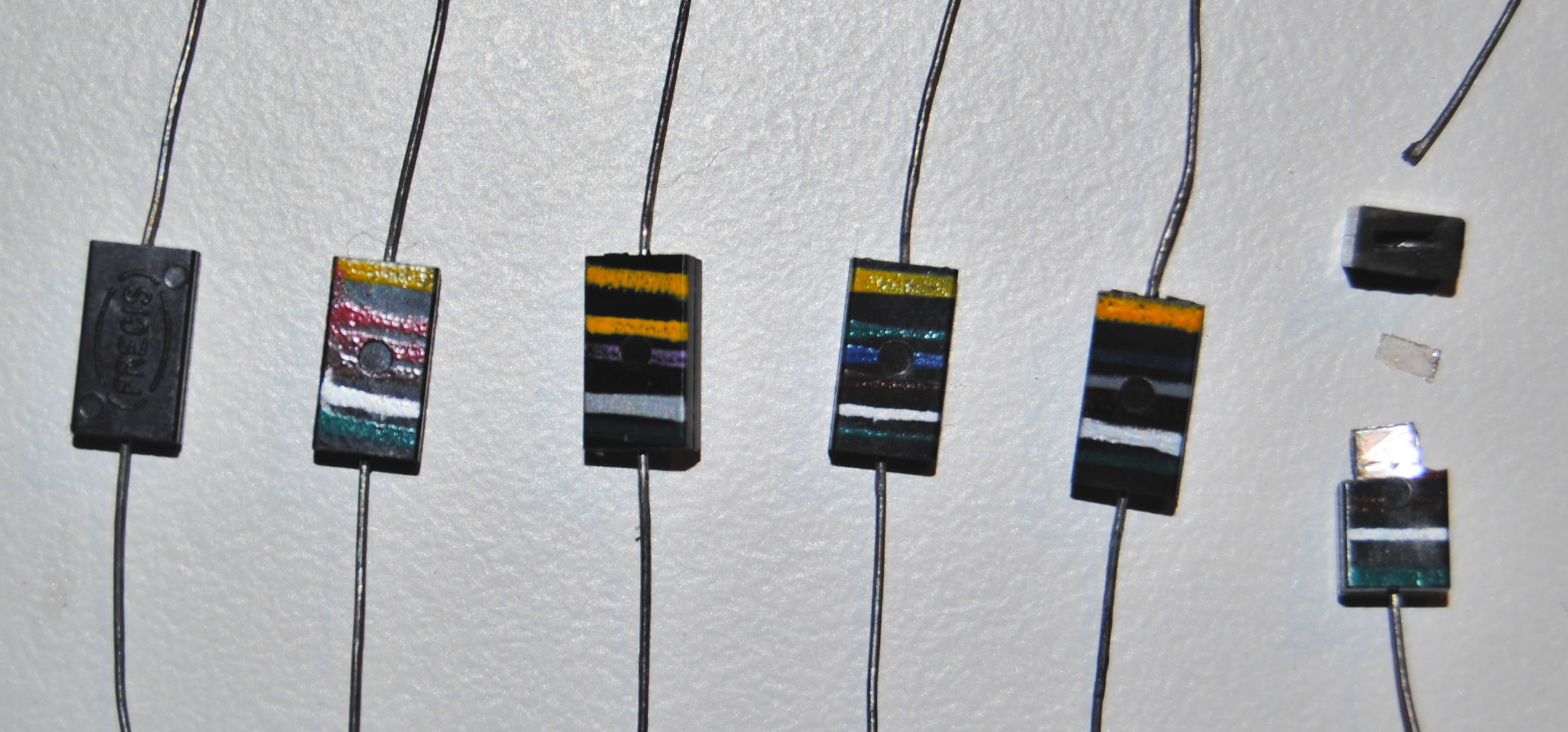 Figure 7 — Molded-mica capacitors marked with painted colour stripes; the rightmost is cracked open, exposing the mica dielectric. Source: Wikimedia Commons, user Hypesnave, CC0.