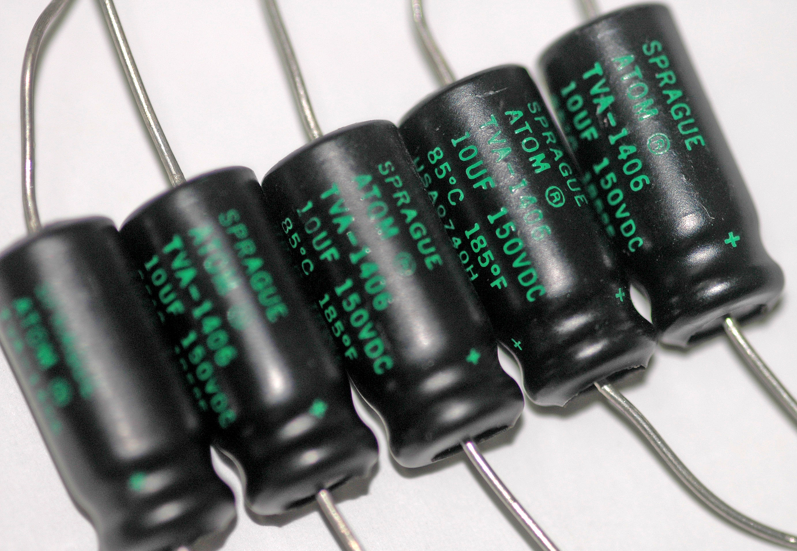 Figure 9 — Axial-lead electrolytics, the older horizontal form: leads emerge from opposite ends of the can. Common in vintage equipment and in tight, flat layouts; the negative stripe and, on many,…