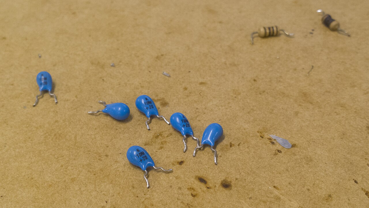 Figure 7 — Through-hole dipped tantalum capacitors that failed short-circuit; the charred, split bodies are the visible aftermath of the ignition sequence. Source: Wikimedia Commons, WizardTim (CC …