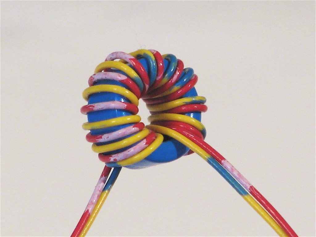 Figure 9 — A hand-wound toroidal choke: the turns are threaded one at a time through the ring. The distributed single-layer winding shown here keeps leakage and stray capacitance low. Source: "Coil…
