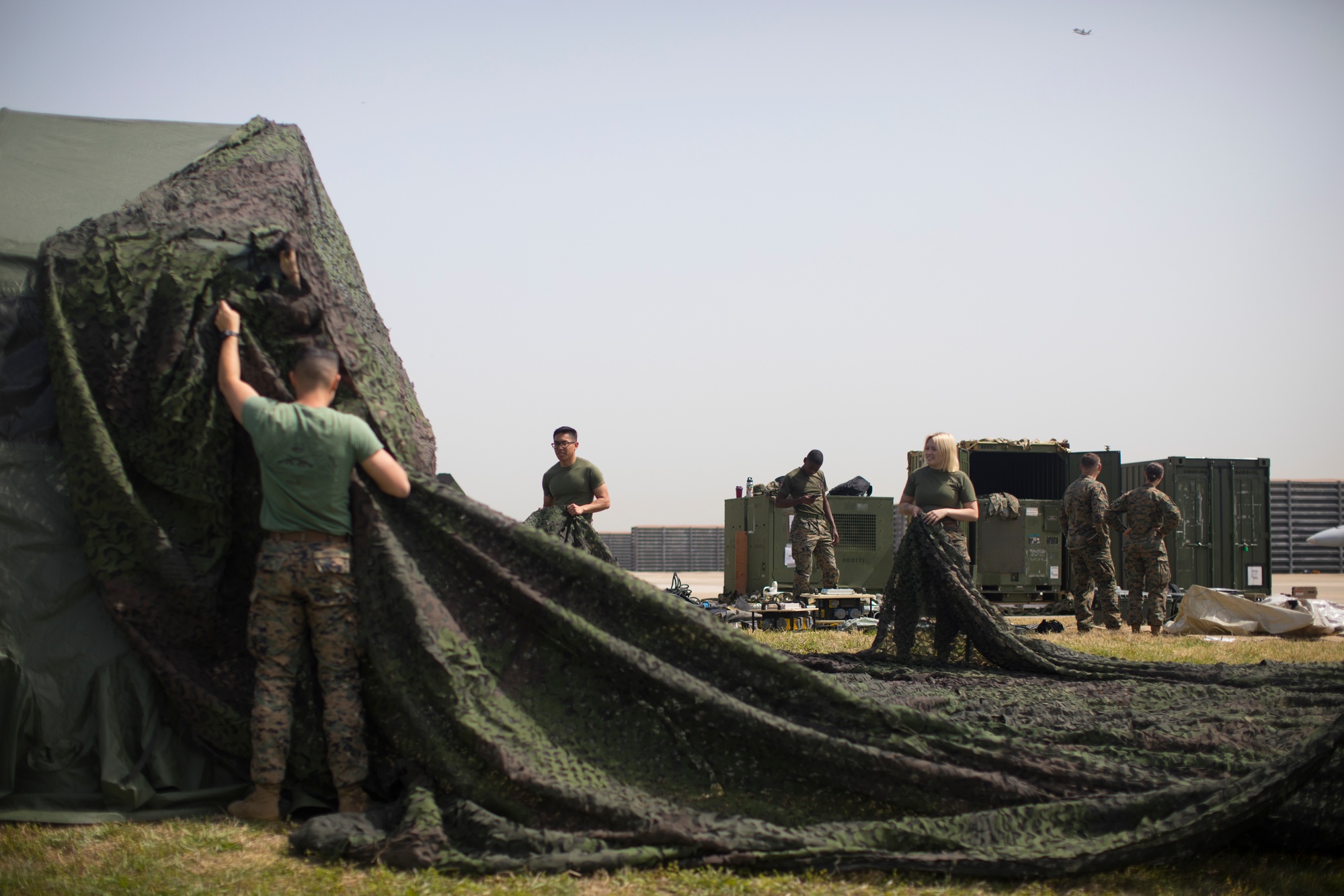 Figure 5 — The same T-SCIF setup, with Marines preparing camouflage netting. Cover and concealment substitute for the below-grade siting or the shielded shell of a fixed facility; the perimeter and…